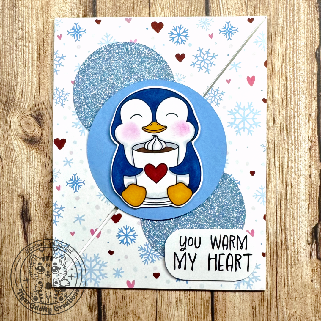 Penguin Card(1) Card featuring penguin holding a cup of hot cocoa with a heart on it on top of blue circles placed diagonally, on top of hearts and snowflakes background DSP. Sentiment says: You Warm My Heart